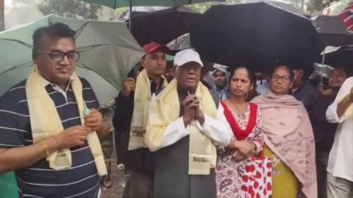 Sankar Malakar campaigns with an umbrella at a tea garden in Bagdogra, interacting with workers despite steady rain. Tuesday, 24 March 2026.